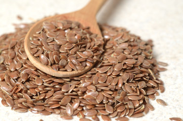 Close up flax seeds in the wooden spoon on a linen textile