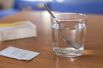 Glass of water with spoon inside to take medicine soluble on wooden table