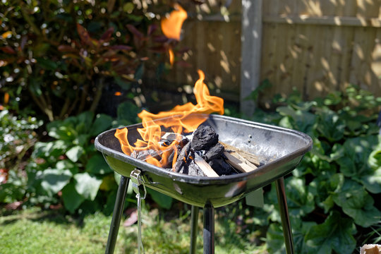 Preparing barbecue party in a garden. Burning charcoal with firestarter and wood.