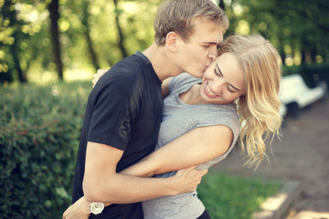 Happy young couple. Beautiful smiling blonde girl hugging her boyfriend in summer park.