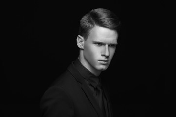 Fototapeta premium Fashion style studio portrait of young calm fashionable man in black costume on black backgound. Young male model with red hair