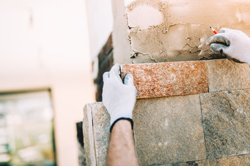 worker installing stone tiles in construction site. masonry details on exterior wall with trowel putty knife.