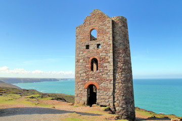Fototapeta na wymiar Derelict abandoned Cornish tin mine building on coast path with sea and blue sky in distance