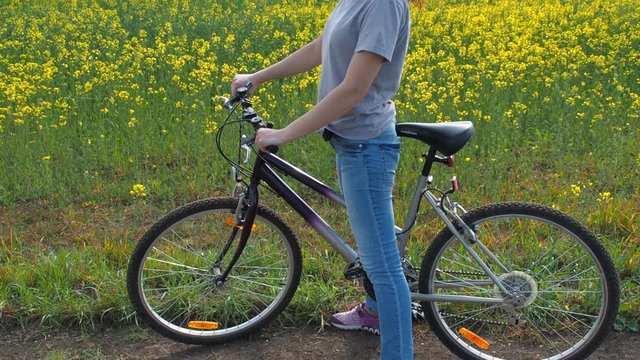 Girl on a bicycle in the nature. A woman is riding a bicycle outside the city. Healthy lifestyle. Rapeseed field. Country road.