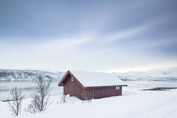 Typical norwegian warm and cozy house located at the lakeside at a fjord in a snowy winter landscape.