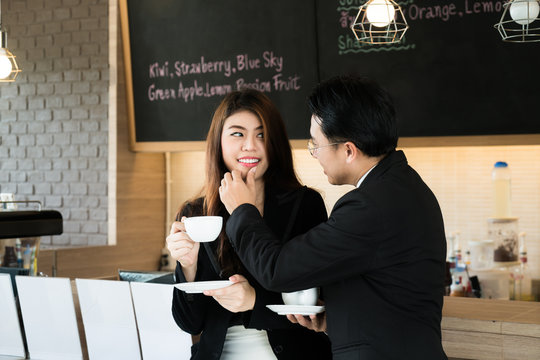 View of Asian business manager touching secretary’s chin with his finger in cafe. Business sexual concept.