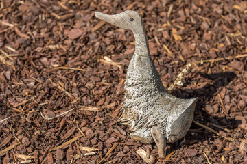 Wood carved duck on a mat of brown chip wood for the garden - side view