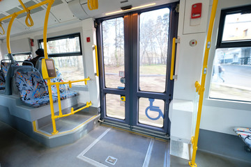 Interior of modern city articulated low floor tram with seats, yellow handles. Wide angle shot of front doors - obrazy, fototapety, plakaty