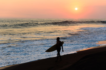 Silhouette of surfer walking on beach at sunset