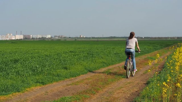 Girl on a bicycle in the nature. A woman is riding a bicycle outside the city. Rapeseed field. Country road.