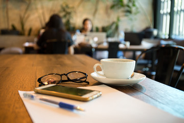 Selected focus coffee cup and glasses with pen and paper on wooden table