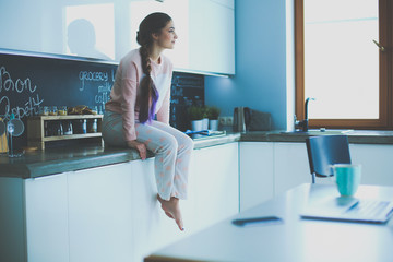 Young woman sitting on table in the kitchen