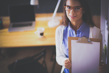 Young woman standing near desk with laptop holding folder
