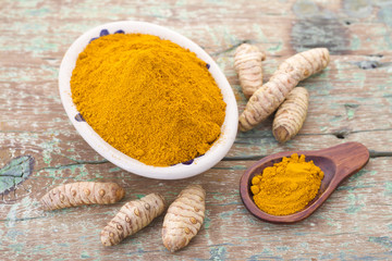 Roots and turmeric powder on wood background (long curcuma)