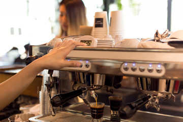 Barista making fresh espresso shot from coffee machine with customer in background