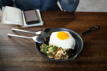 Woman with cell phone having stir fried chicken chilli and thai basil with fried egg on top