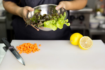 Chef  hand holding bowl of vegetable salad with lemon and carrot