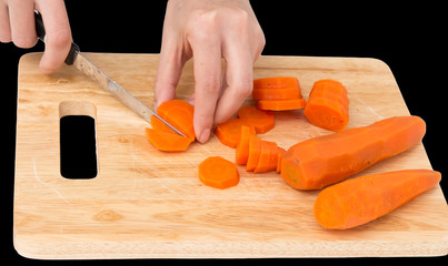 cook cuts carrots on a board on a black background