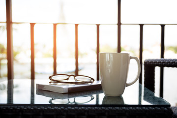 Cup of coffee and reading book with glasses on table with sunlight