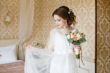 Pretty young Bride.blonde-haired woman with wedding hair-style with a long tail. Boudoir morning of the bride. Looking on her bouquet