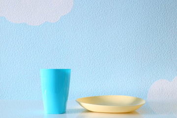 Children's plastic cup and a plate on blue background