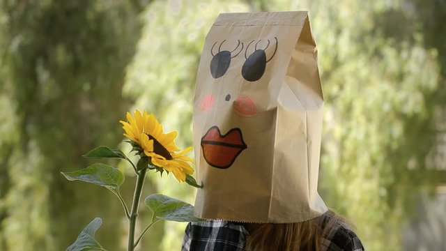 A cute sweet lovely kawaii breadbag face looking at a big yellow sunflower.
