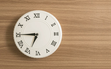 Closeup white clock for decorate show a quarter to seven or 6:45 a.m. on wood desk textured background with copy space