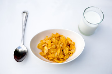 Corn flakes with milk and spoon on white table