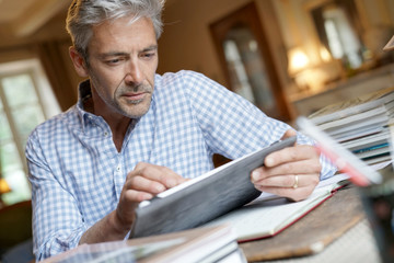 Mature man at home sitting at desk and using digital tablet