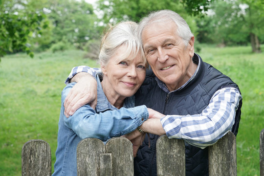 Portrait of senior couple leaning on fence in countryside