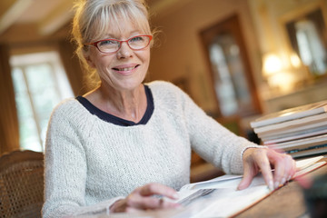 Senior woman sitting at desk and writing on book