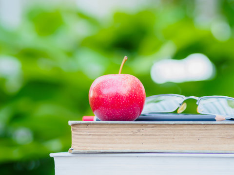 Stack of books, pencil, glasses and red apple on wooden table