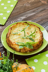 squash casserole decorated by basil leaf and arugula on light green plate at wooden table with squash fruits  and light green napkins at white polka dots pattern