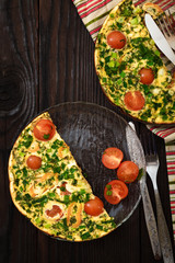 Omelette with greens, tomatoes and sweet pepper for breakfast in a glass plate on a dark wooden table