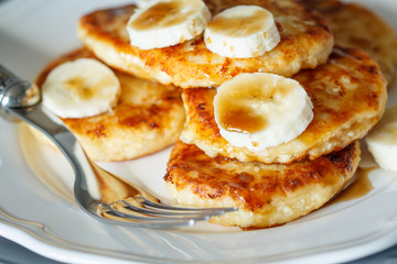Homemade cottage cheese pancakes with caramel (honey) and banana on a white plate.