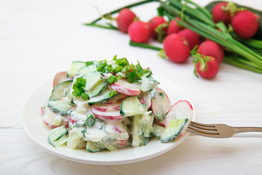 A salad of radish, cucumber and green onions. White woodcock on a white wooden table