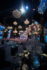 Tall crystal vases with chrysanthemums stand on mirror tables in dark restaurant hall