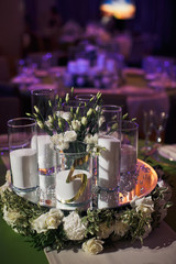 White candles stand on tray with flowers in the middle of green table