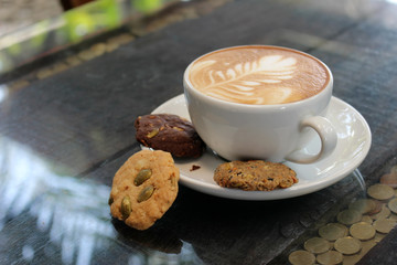 Latte coffee with flower art and biscuits on the saucer