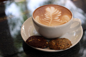 Latte coffee with flower art and biscuits on the saucer