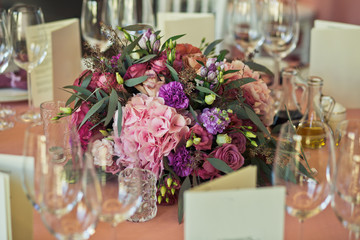 Glasses stand aroung pink bouquet in the middle of dinner table