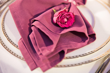 Pink rose bud lies on dark pink serviette on dinner plate