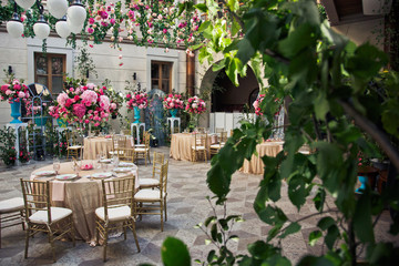 Look from behind green bush at beige tables standing in the hall