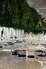 Violet chairs stand at white dinner tables under large festoon of greenery