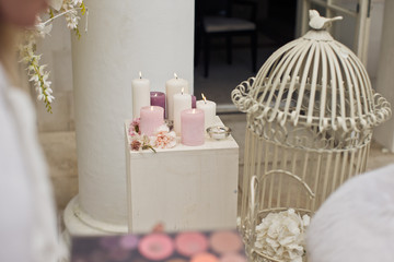 Violet and pink candles stand on the pillar before bird cage