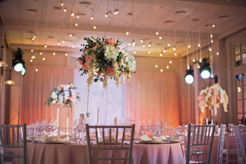 Round dinner table covered with pink cloth and decorated with beautiful flowers in tall vase