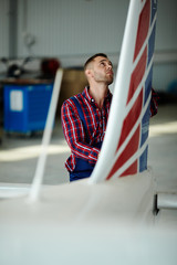 Airplane service crew working on preflight maintenance: Portrait of handsome mechanic inspecting fuselage of jet plane in hangar