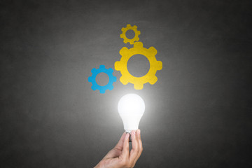 Human hand holding light bulb with gears.