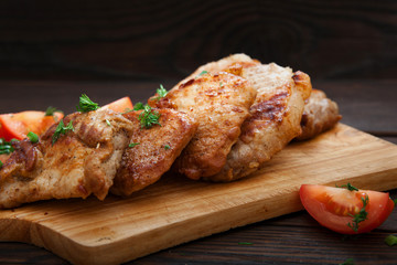 Sliced grilled pork barbecue meat on wooden cutting board over dark background