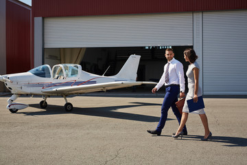 Portrait of two smiling business people, man and woman, walking by plane hangar in airport field